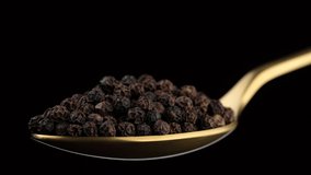 black pepper in golden spoon isolated on black background. Flavorful and aromatic peppercorn. 4K UHD video