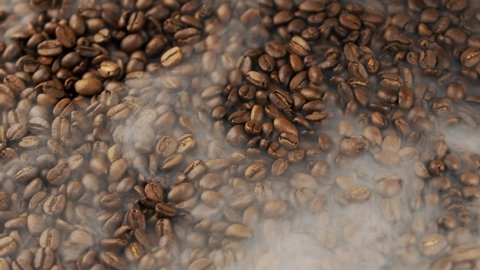 Roasted Coffee Beans falling. smoke comes from coffee beans. Fragrant coffee beans are roasted  Slow motion. Rotating camera. Organic coffee seeds.