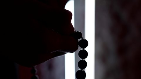 woman is holding rosary beads, dark silhouette of female hands against light, closeup view