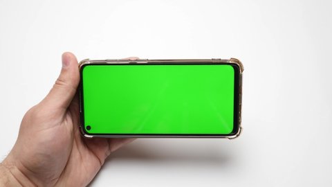 A male hand holds a phone with a green screen and turns the pages. On a white background