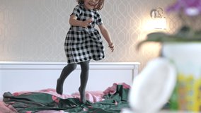 Happy little girl jumps on the bed in her parents' bedroom. Beautiful baby having fun in bed jumping. Slow motion 4K video of children smiling.