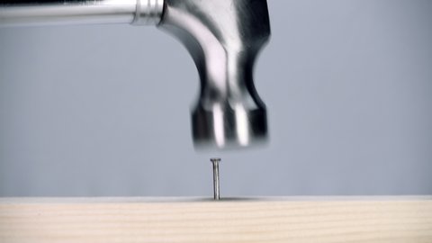 New shiny chrome hammer drives a nail into a wood plank. Macro. Closeup