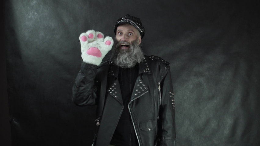 Bearded rocker in leather jacket and cap smiling and waving to audience with white cat paw glove on nightclub stage concert with black curtain background Royalty-Free Stock Footage #1071195640