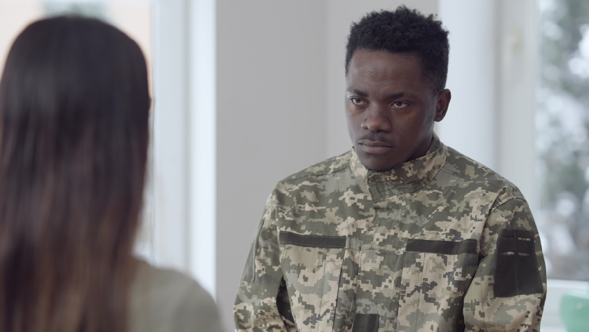Portrait of young handsome African American man in army uniform hugging Caucasian woman looking away. Sad soldier leaving wife. Upset husband embracing spouse at home