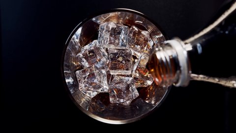 Pouring Cola with ice cubes. Top view of rotating glass with Ice and bubbles in glass. Soda closeup. Food background. Rotate glass of Cola. Camera moving. Slow motion 4K video footage. Macro Shot.