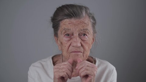 Very old Caucasian senior woman 90 years old with deep wrinkles and gray hair fitted dental prosthesis on gray wall background in studio. Elderly female inserts denture. False teeth. Dental concept