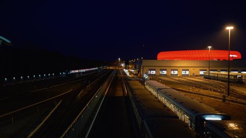 MUNICH, GERMANY - Apr 01, 2021: Allianz Arena, home venue of FC Bayern Munich, illuminated in the evening  The overground subway enters the station "Freimann" at night 