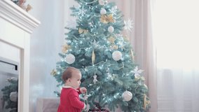 authentic cute happy Joy chubby infant girl wearing santa hat and red dress smile play have fun celebrating new year festive atmosphere near christmas tree at home. Childhood, hollyday, winter concept