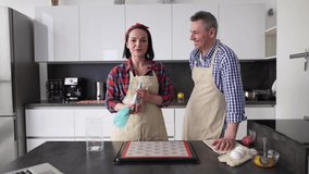 Positive couple at kitchen making macaroons at home, talking on camera