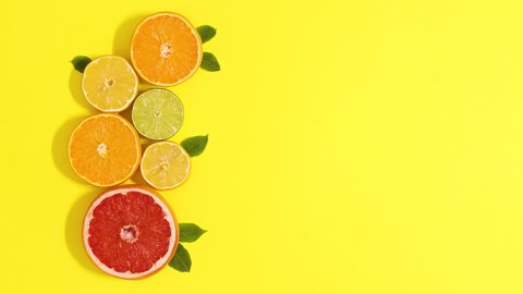 6k Fresh citrus fruits with green leaves appear on left side of yellow background. Stop motion flat lay
