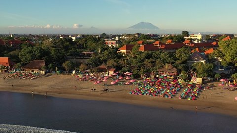Aerial drone footage of the famous Seminyak beach, lined with beach bars, with the Agung volcano in the background in Kuta, Bali, Indonesia