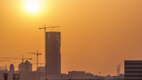 A tower in Doha timelapse under construction, silhouetted against the sunset. Close up view with many cranes, Qatar