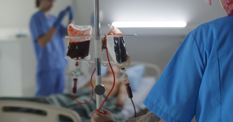 Blood transfusion to young male patient in hospital room. Nurse pushing iv set with blood for unconscious man lying in hospital bed in intensive care unit