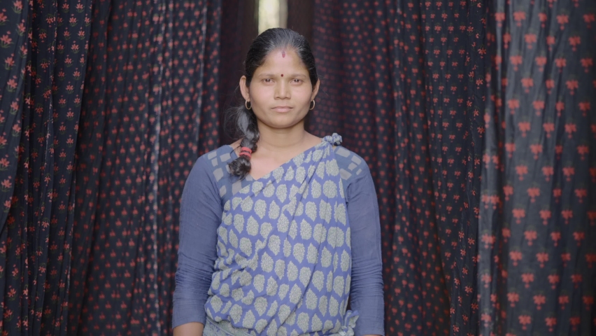 Close up shot of an Indian female daily wage laborer of  local or domestic textile dyeing firm standing around the color printed cloth materials for the drying process smiling and looking at Camera | Shutterstock HD Video #1071212932