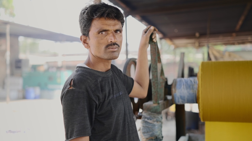 Outdoor shot of an Indian middle-aged male local textile factory laborer standing by running the machinery of cloth sheets and looking at the camera in a broad daylight Royalty-Free Stock Footage #1071212938