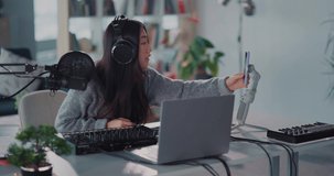 Asian attractive girl wearing headphones and playing electronic music with piano synthesizer enjoying videochat online with social media audience.