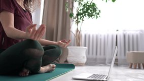An attractive girl completes a set of ogi exercises while sitting on a yogamat near a laptop. Online yoga lesson. 4K