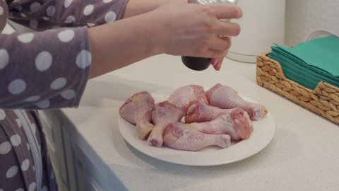 Woman preparing food in the kitchen cooking chicken drumsticks sprinkling chicken meat with ground pepper, using pepper mill. High quality 4k footage