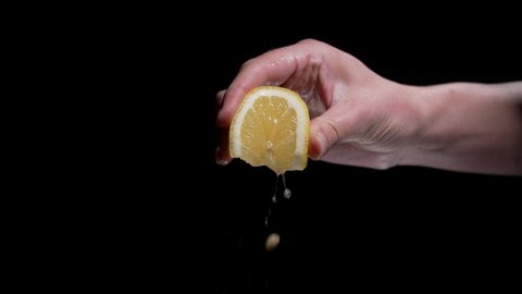 This slow motion video shows an anonymous hand squeezing a juicy lemon wedge against a black background.