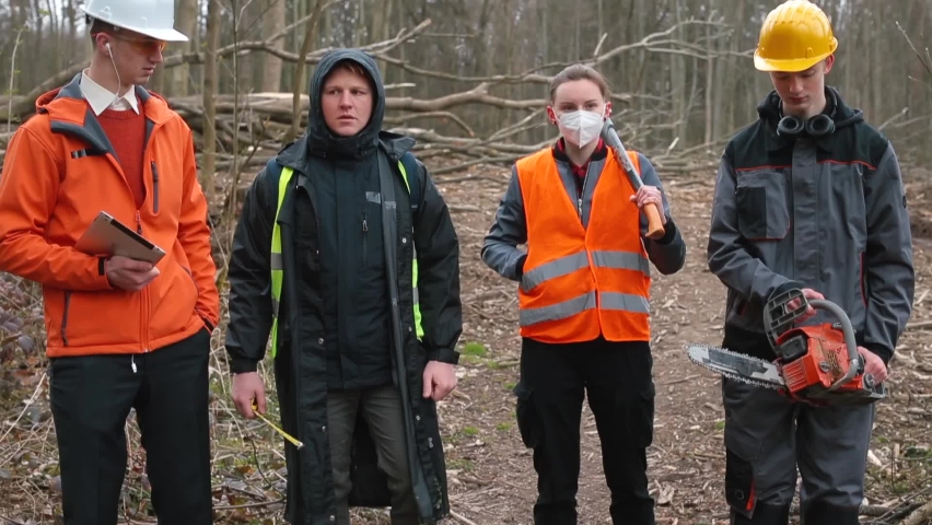 Group logging workers moving through forest. They hold tools, an ax, saw, tablet in their hands. Discussion work issues in team workers. Communication. End of the working day.