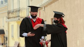 A classmates in graduation gowns and caps making selfie photo with mobile phone at the street . Class of 2021.