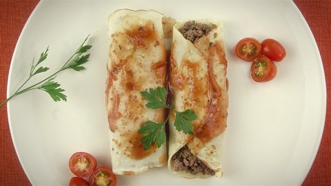 Pancakes with meat, in tomato sauce and cheese, with cilantro and grated cheese on top, and some cherry tomatoes on the plate. Top view.