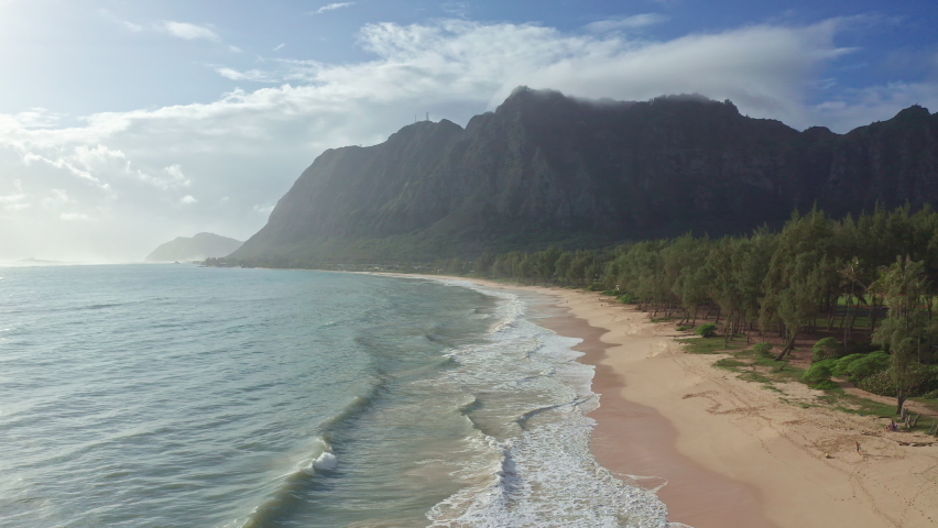 Colorful aerial view of rocky mountains. A tropical beach with turquoise blue ocean water and waves lapping on a hidden white sandy beach. Waimanalo Beach, Oahu Island, Hawaii.