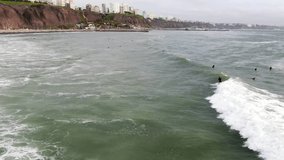 4k daytime aerial video following a surfer riding a wave on the coastal waters of the Pacific Ocean in Lima, capital city of Peru.