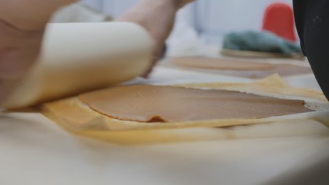 the male hands of a Caucasian pastry chef roll the brown dough with a rolling pin with a white rolling pin. Trim the dough into a circle for the biscuit honey cake layer