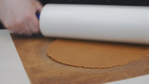 pastry chef baker rolls out brown dough on a brown rug on the table with a large white rolling pin. The baker cuts the flat cake in a round metal shape. Removes excess dough