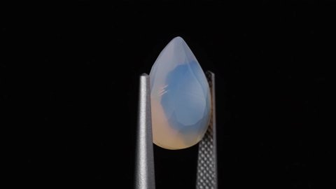natural opal gemstone in the tweezer on the background