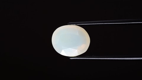 natural opal gemstone in the tweezer on the background