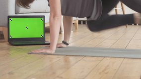 Young woman's workout at home. Her laptop has green screen and marks for you to track.