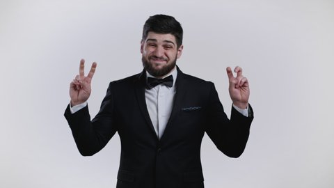 Handsome man showing with hands and two fingers air quotes gesture, bend fingers isolated on white background. Guy in black tuxedo. Not funny, irony and sarcasm concept.