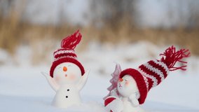Close-up view. Happy snowman toys in red knitted hats stands on the snow around pink Christmas tree shaped candle. 4K resolution video. Christmas ornaments theme.