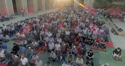 Bukhara, Uzbekistan - 6 15 2018: Morning namaz (muslim prayer) in the Kalyan Mosque of Bukhara filmed by drone cam. Many kneeling people are sitting in the courtyard of the mosque. 