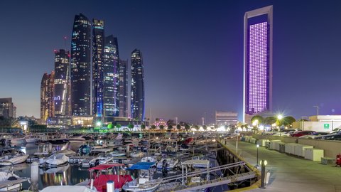 Al Bateen marina Abu Dhabi day to night timelapse after sunset with boats in harbor and illuminated modern skyscrapers on background
