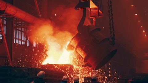 Pouring bright hot liquid steel or metal from ladle in blast furnace foundry metallurgical factory. Steel mill iron smelting process with bright sparks and smoke
