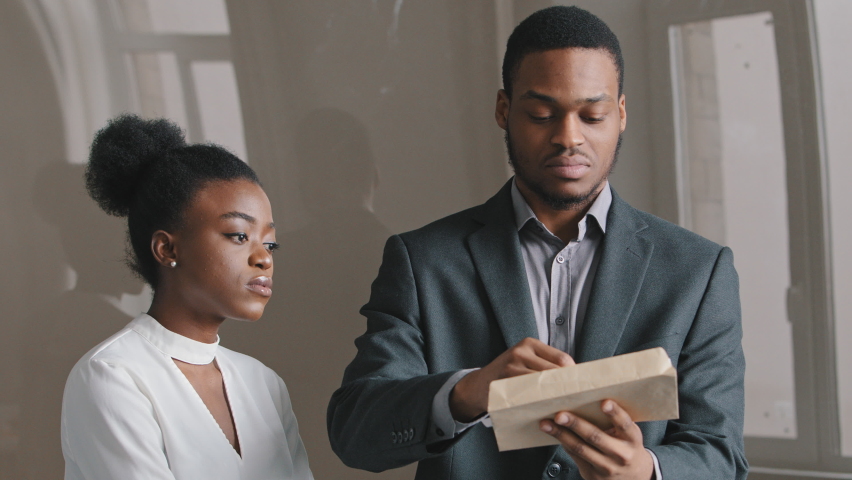 Concentrated 25's African American young man holding paper document feeling unhappy with negative news. Disappointed employee receives notice of dismissal from boss. Sad desperate woman losing job Royalty-Free Stock Footage #1071262897