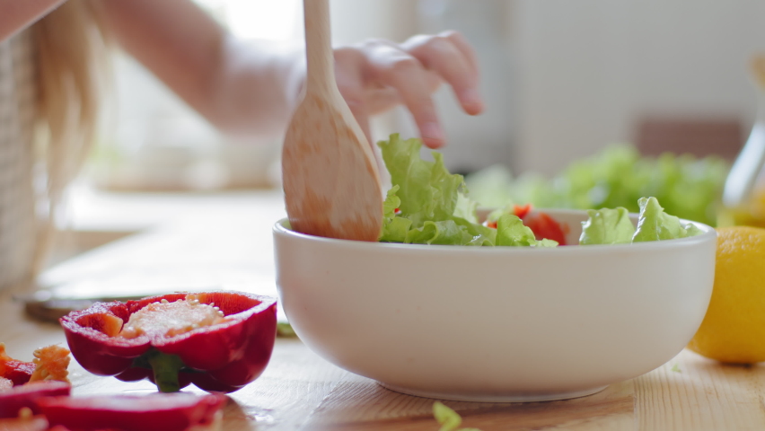 Close-up female hands stirring with wooden spoon ingredients vegetables in fresh delicious salad, unrecognizable family mother and daughter vegetarians prepare meal dish with red pepper green leaves Royalty-Free Stock Footage #1071262933