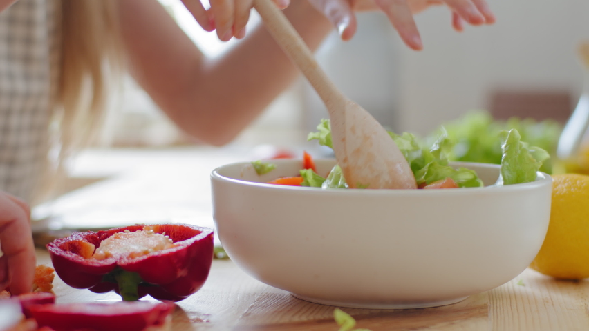 Close-up female hands stirring with wooden spoon ingredients vegetables in fresh delicious salad, unrecognizable family mother and daughter vegetarians prepare meal dish with red pepper green leaves Royalty-Free Stock Footage #1071262933
