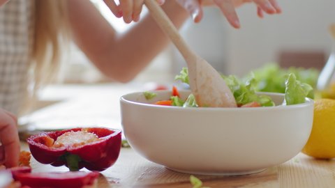 Close-up female hands stirring with wooden spoon ingredients vegetables in fresh delicious salad, unrecognizable family mother and daughter vegetarians prepare meal dish with red pepper green leaves