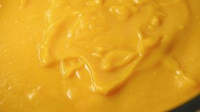Cream of roasted pumpkin soup recipe. Step 22. Close-up view of person pouring liquid cream into almost ready pumpkin cream soup. Side view. Slow motion video. Home cooking theme.
