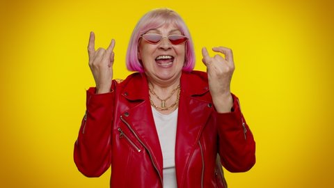 Overjoyed elderly granny woman rocker showing rock n roll gesture by hands, cool sign, shouting yeah with crazy expression, dancing, emotionally rejoicing in success. Senior mature old grandmother