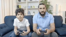 Dad and son playing video game together, upset with loss, family leisure