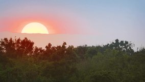 Huge orange ball of the sun. sets slowly in a hazy sky. over the wilderness in Yala National Park. Sri Lanka