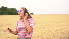 Slow motion tracking video clip of pretty blonde girl teenager young woman wearing a striped t- shirt and blue sunglasses walking listening to music on her cell phone and wireless headphones