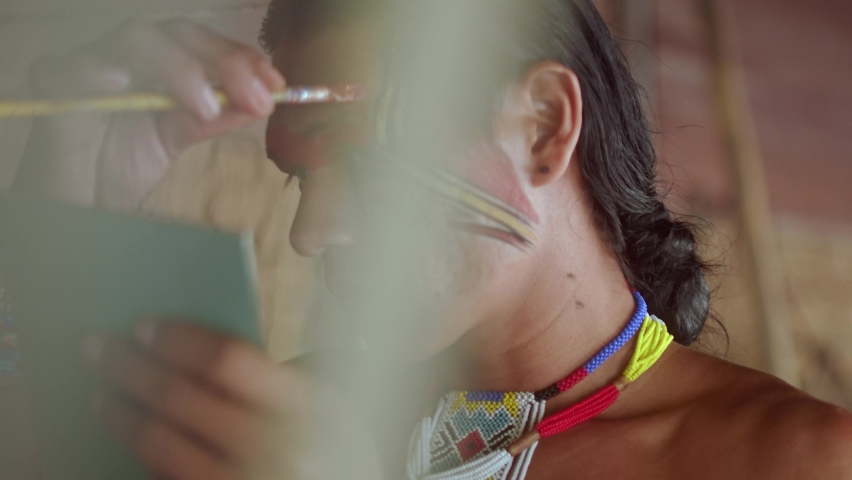 Indian from the Pataxó tribe, using a mirror and doing face painting. 6K.