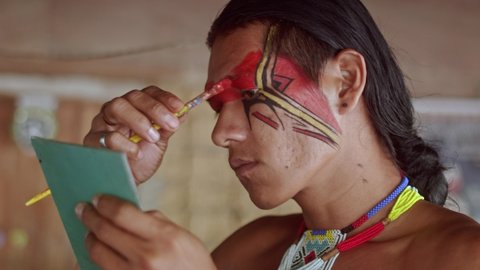 Indian from the Pataxó tribe, using a mirror and doing face painting. 6K.