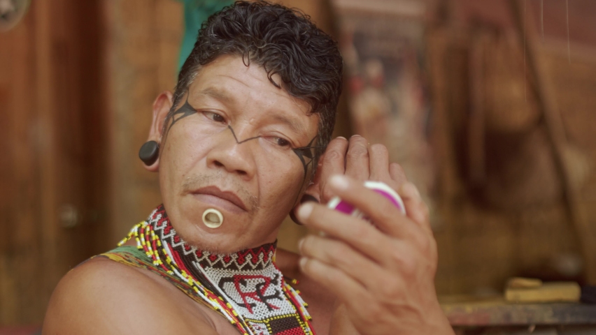 Indian from the Pataxó tribe, using a mirror and doing face painting. 6K.